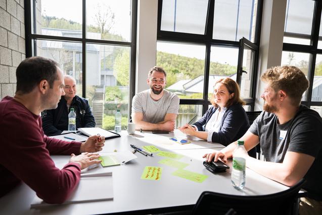 5 Personen in einem Tagungsraum sitzen am Tisch und arbeiten